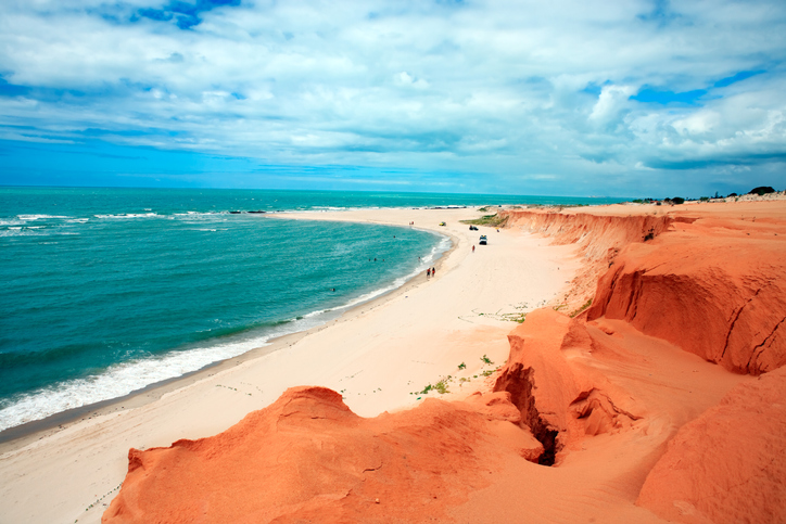 Na imagem vemos Canoa Quebrada, no Ceará, Brasil, em um dia ensolarado. O mar azul e as falésias avermelhadas.