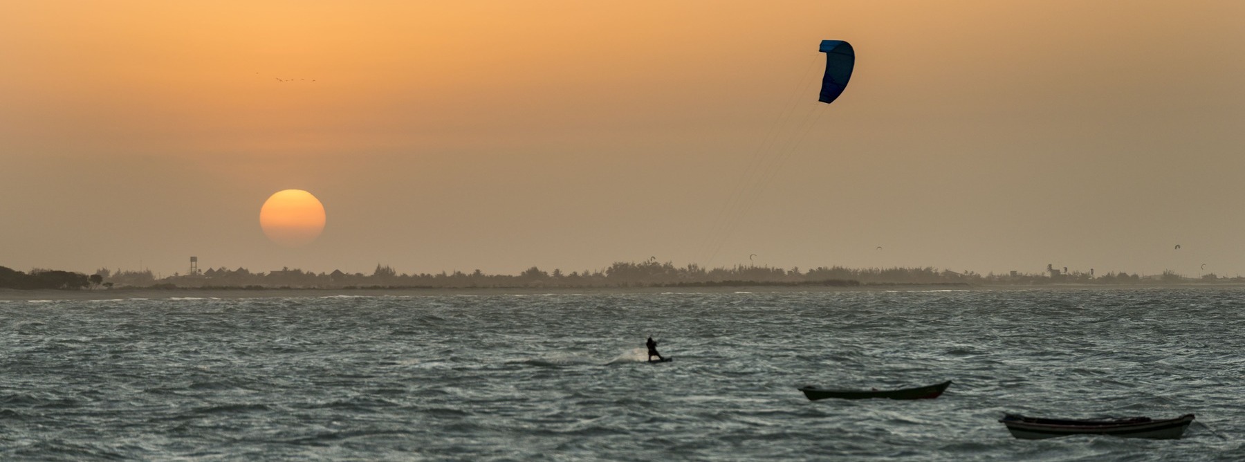 Fim de tarde em Barra Grande, Piauí. Por do sol e praticante de kitesurf no mar. Pequenos barcos flutuando.
